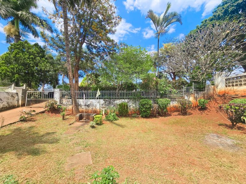 A spacious garden area featuring mature trees, established landscaping, and secure metal perimeter fencing with a gated entrance.