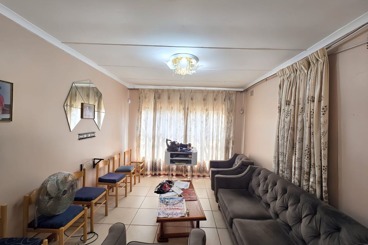 A living room featuring tiled flooring and a central ceiling light fixture, with large windows covered by curtains.