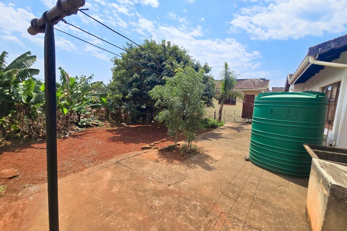 Rear exterior area featuring a concrete paved yard, water storage tank, and utility wash basin, set against a garden space.