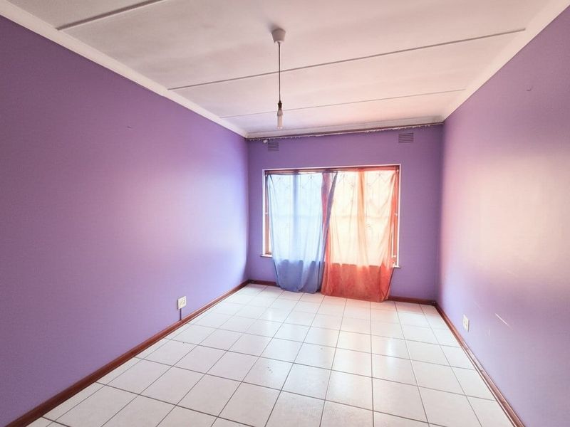 An empty bedroom featuring tiled flooring, ceiling vents, and a simple pendant light fixture, ready for a fresh coat of paint and new decor.