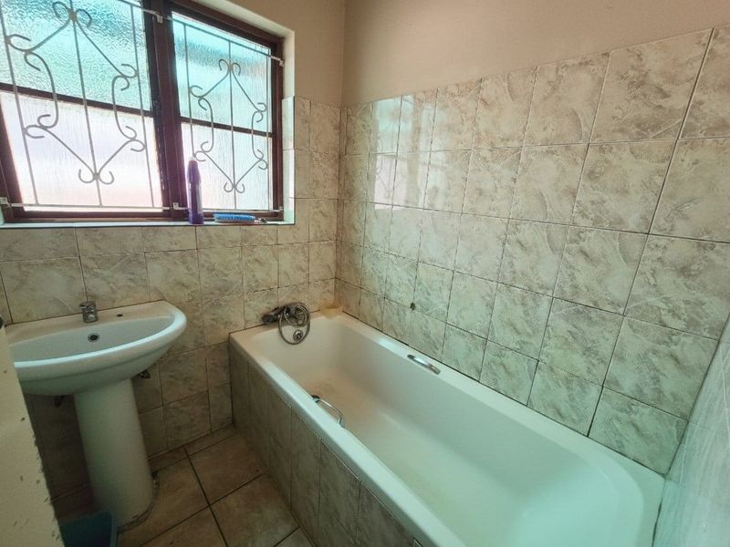 A dated bathroom featuring a pedestal basin, bathtub, and tiled finishes, requiring cosmetic updates to modernize the space.