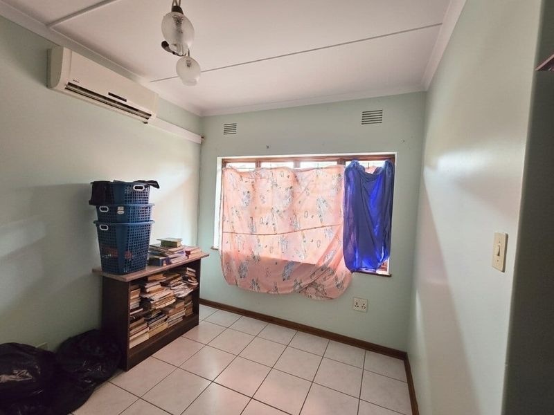 A bedroom featuring tiled flooring, a wall-mounted air conditioning unit, and a window with natural light.