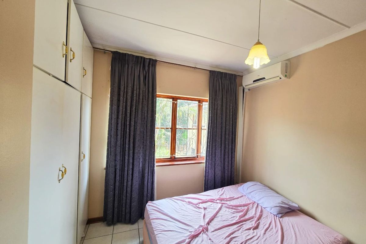A functional bedroom featuring built-in cupboards, tiled flooring, and an air conditioning unit for climate control.