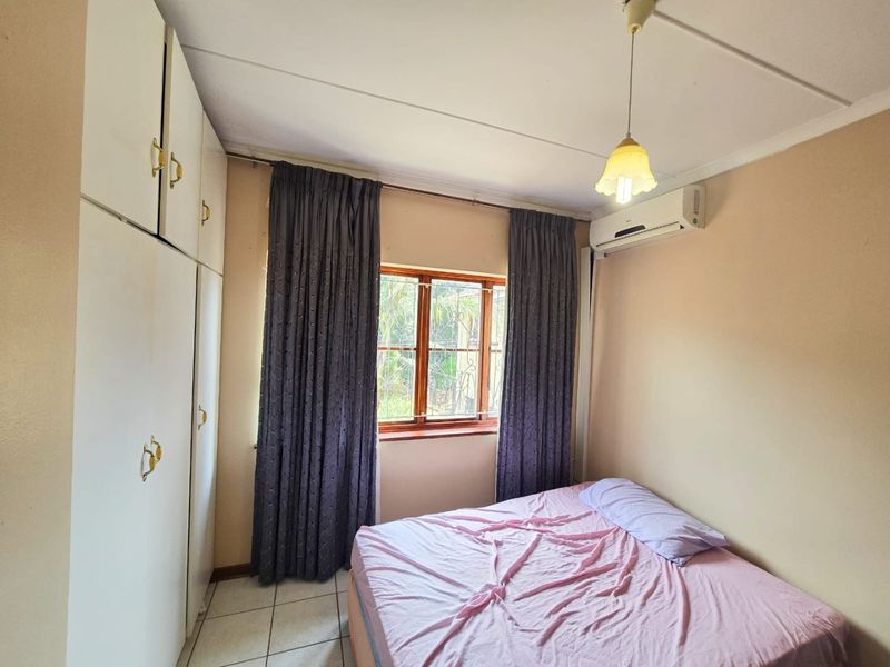 A functional bedroom featuring built-in cupboards, tiled flooring, and an air conditioning unit for climate control.