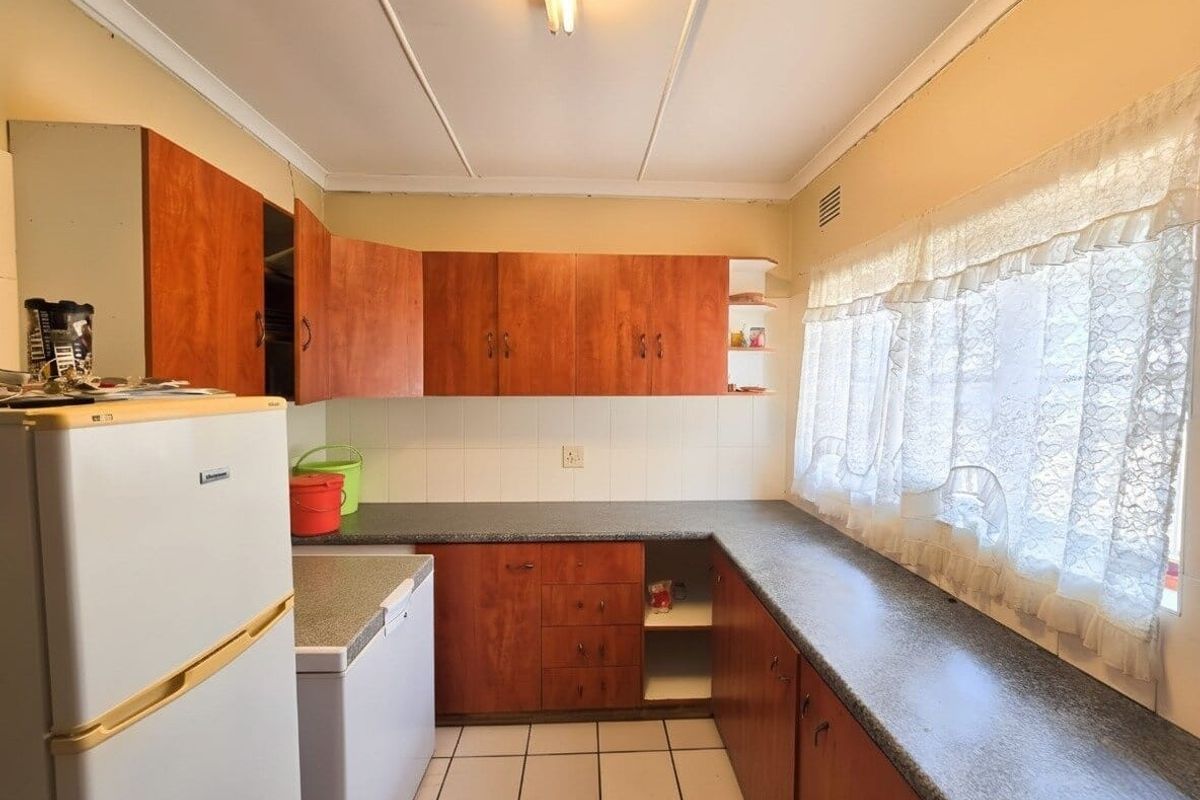 A dated kitchen featuring wood-look laminate cabinetry, tiled flooring, and a tiled backsplash, offering potential for a modern renovation.