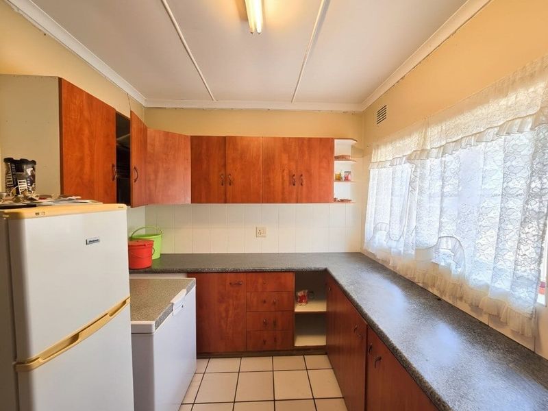 A dated kitchen featuring wood-look laminate cabinetry, tiled flooring, and a tiled backsplash, offering potential for a modern renovation.
