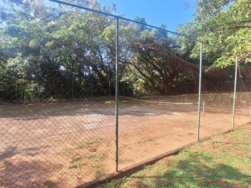 An outdoor clay tennis court enclosed by chain-link fencing, showing signs of significant wear and lack of maintenance.