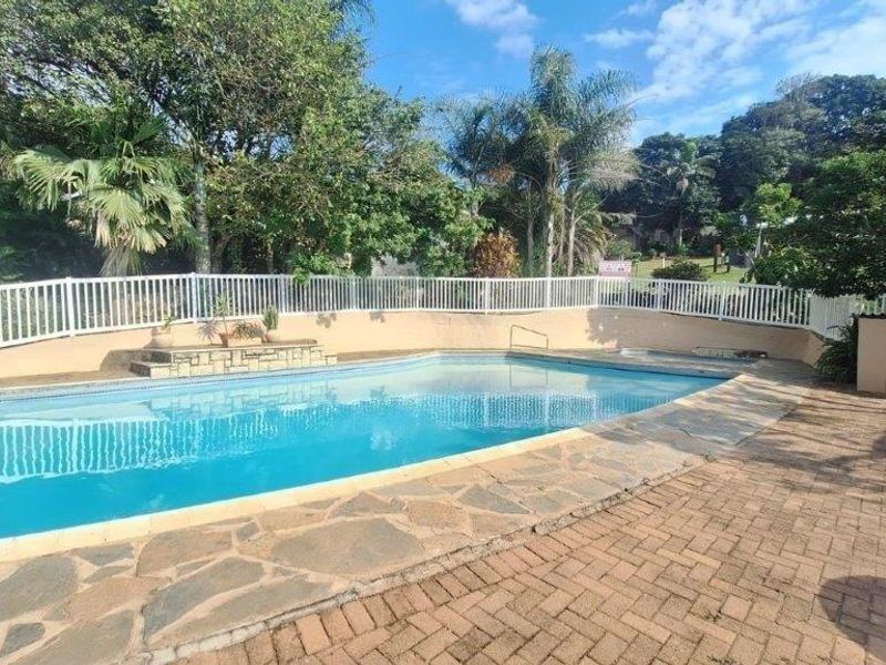 Outdoor swimming pool area featuring paved surround, perimeter fencing, and established garden surroundings.