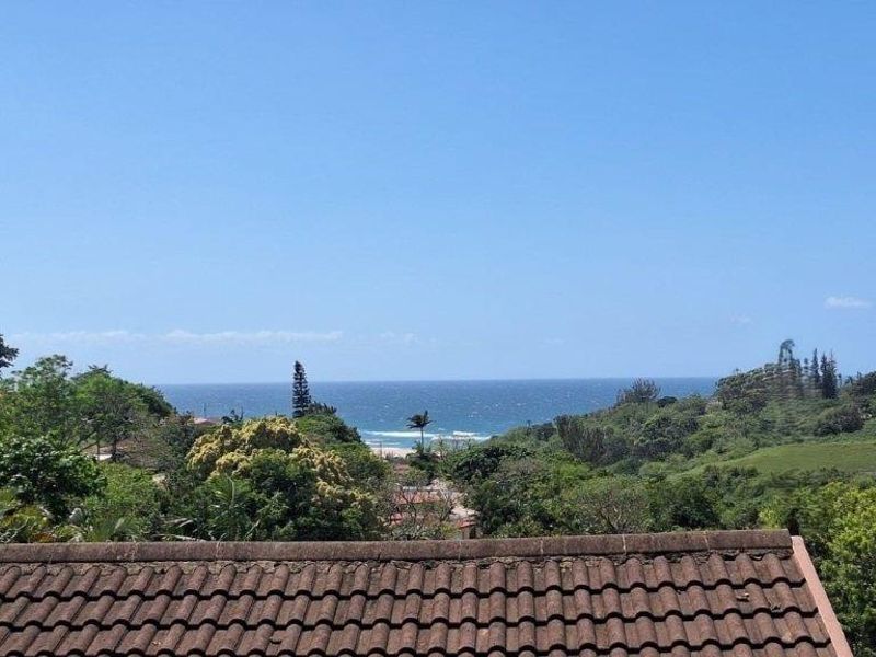 Elevated view overlooking lush green landscape and the ocean horizon, featuring a tiled roof in the foreground.