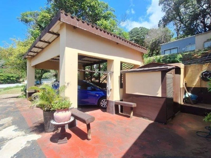 A covered carport area with an attached storage unit and concrete flooring, providing sheltered parking space for the townhouse.