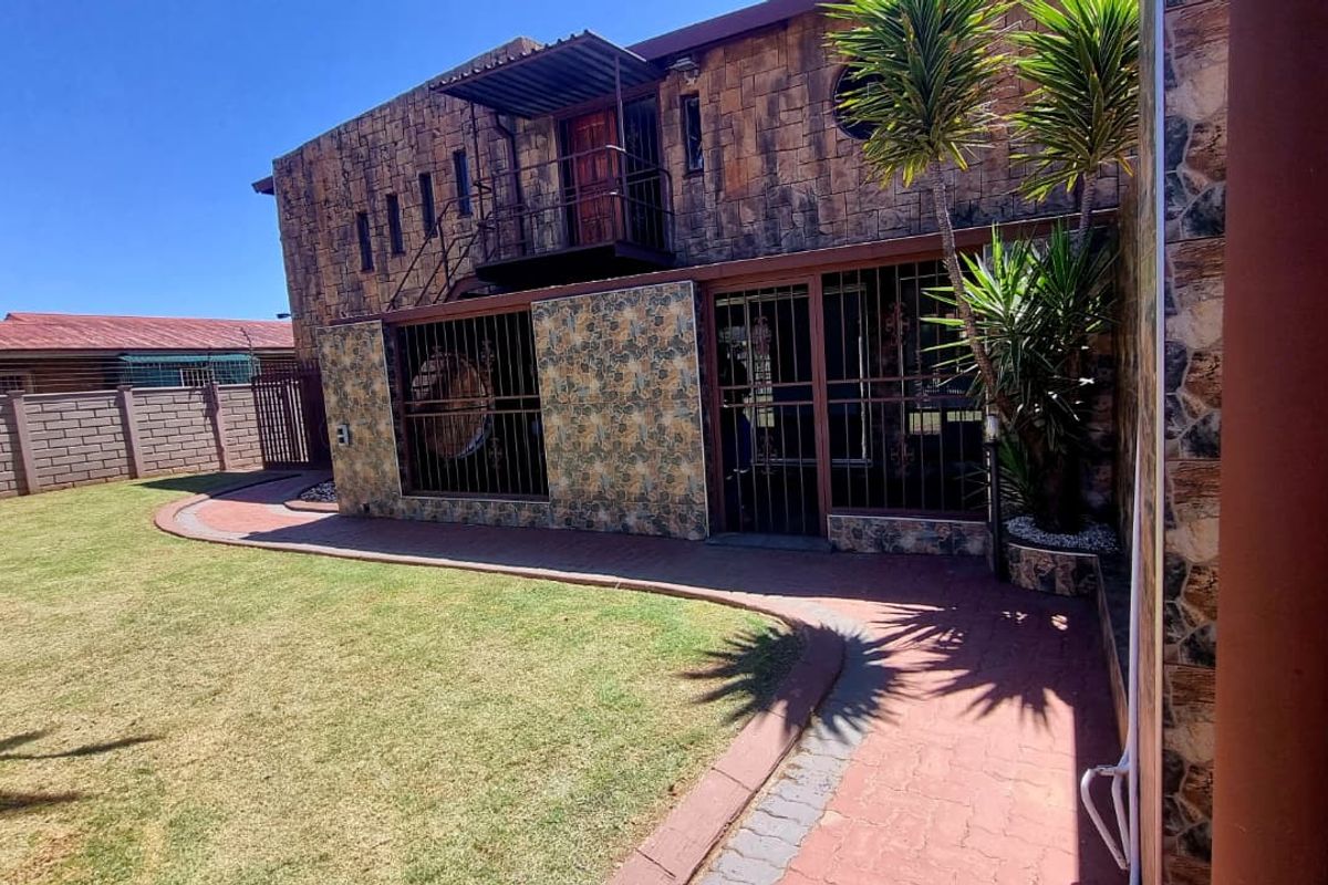Rear exterior view of a two-story house featuring stone cladding, a paved walkway, and a private garden area with security bars on windows.
