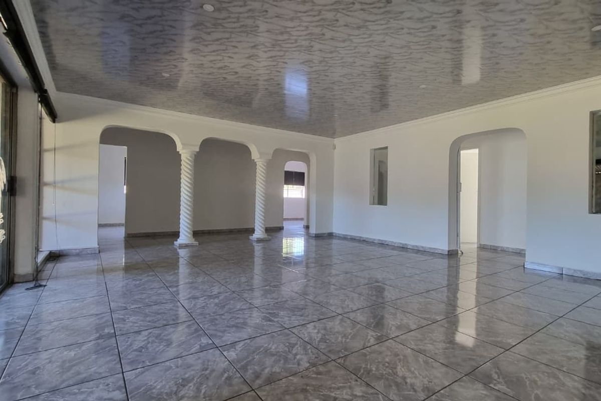 Spacious, empty living area featuring polished tiled flooring, decorative columns, and arched doorways leading to adjacent rooms.