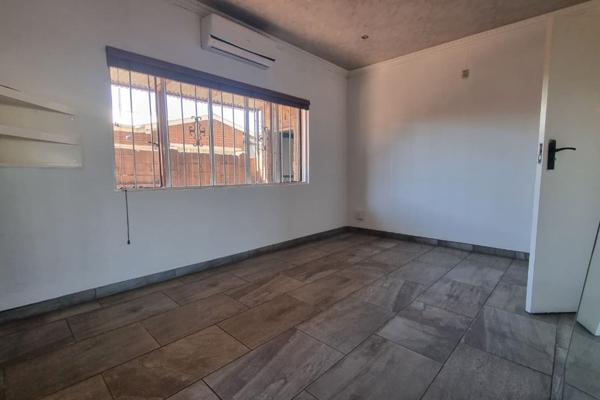 A clean, empty bedroom featuring modern tiled flooring, a split-system air conditioner, and security bars on the window.