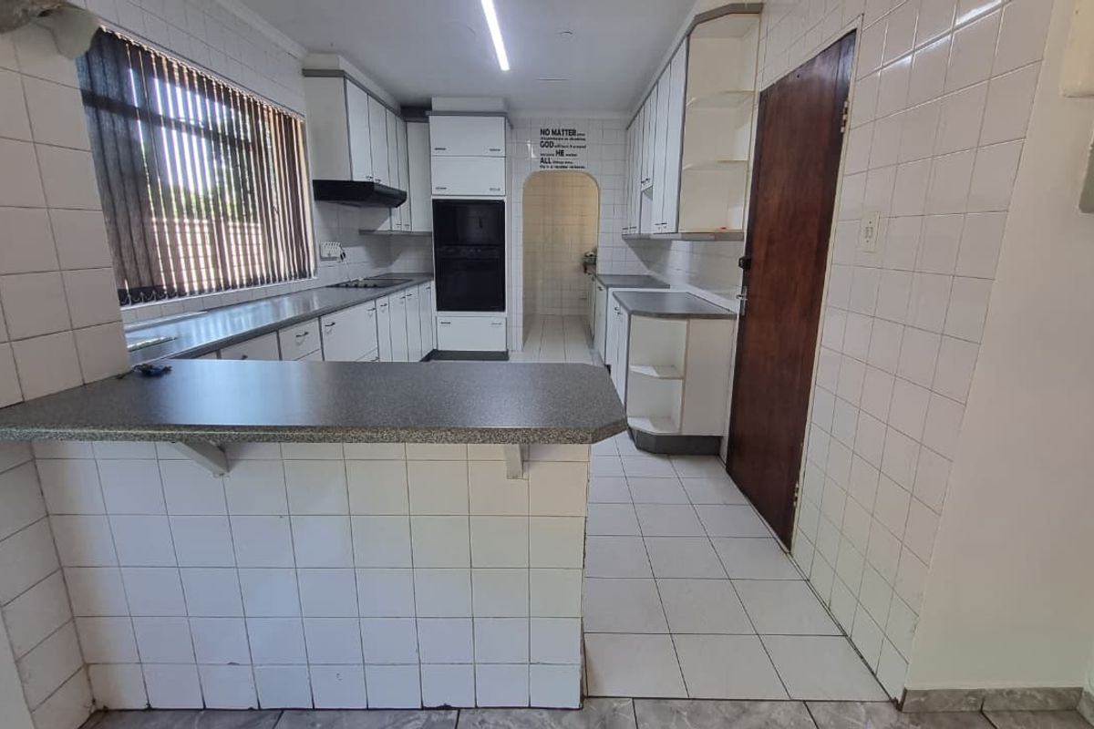 A functional kitchen featuring white built-in cabinetry, laminate countertops, a built-in oven, and tiled flooring with a breakfast bar area.