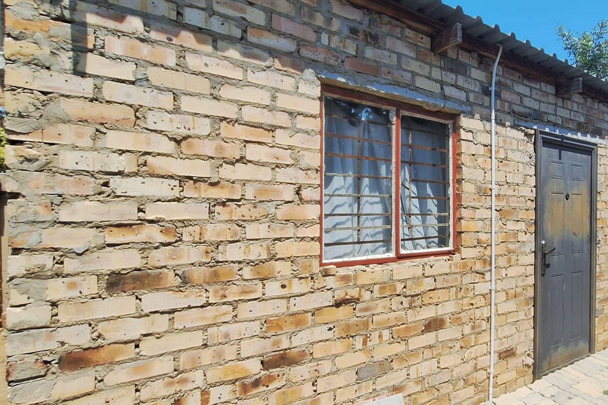 Exterior view of a townhouse featuring exposed brick walls, a metal security door, and a corrugated roof structure.