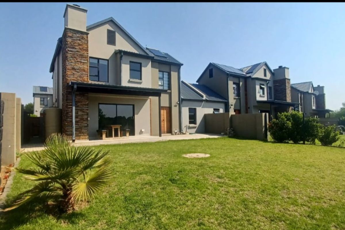 Rear view of a modern townhouse featuring a paved patio area, stone-clad chimney stack, and a well-maintained private garden.