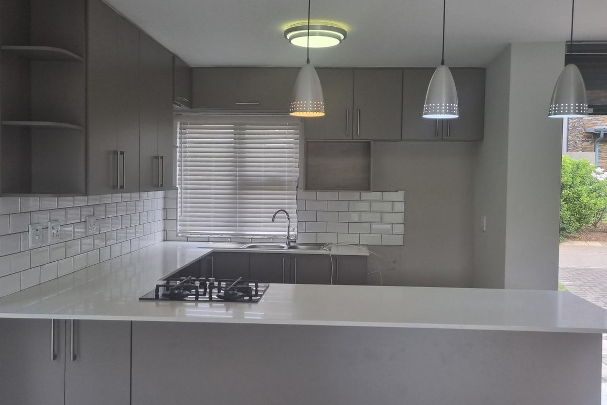 Modern kitchen featuring sleek grey cabinetry, white stone countertops, subway tile backsplash, and a built-in gas hob with breakfast bar seating.