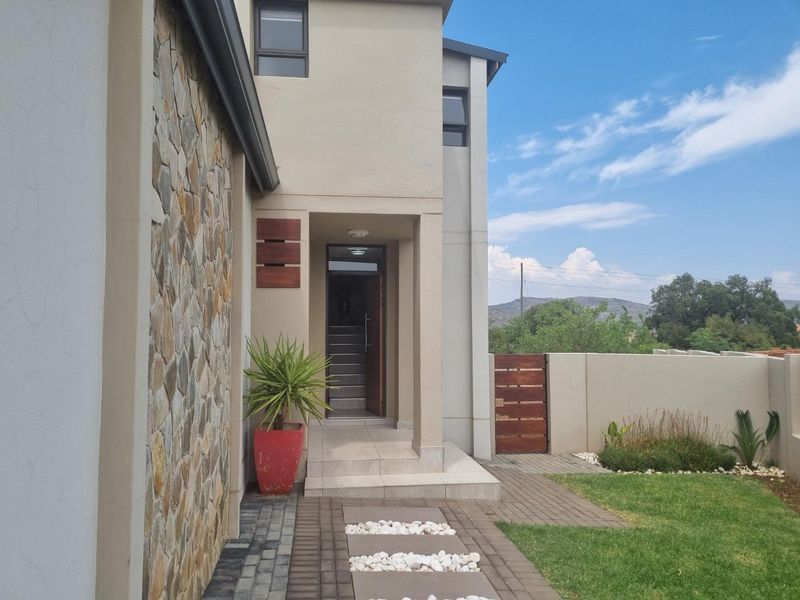 Modern front entrance featuring stone cladding, a paved walkway, and a secure boundary wall with a timber gate.