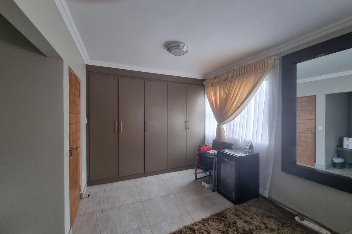 A bedroom featuring neutral tiled flooring, extensive built-in cupboards, and a large wall-mounted mirror, offering a clean and functional living space.