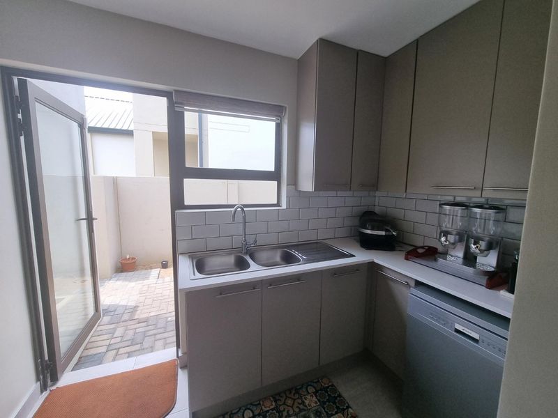 A functional scullery featuring modern cabinetry, a double sink with mixer tap, subway tile backsplash, and direct access to an outdoor paved area.