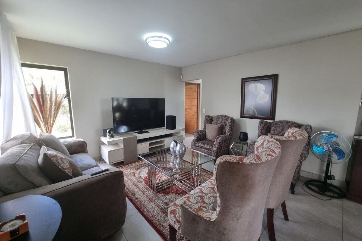 A comfortable living room featuring neutral wall tones, tiled flooring, and a functional layout with access to an adjacent room.