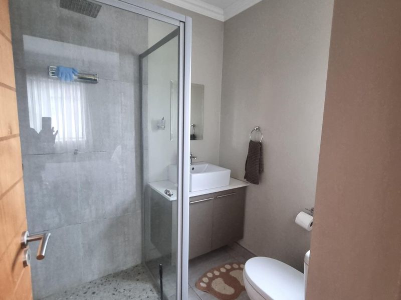 A modern bathroom featuring a glass-enclosed shower, a contemporary vessel sink with a vanity cabinet, and a standard toilet.