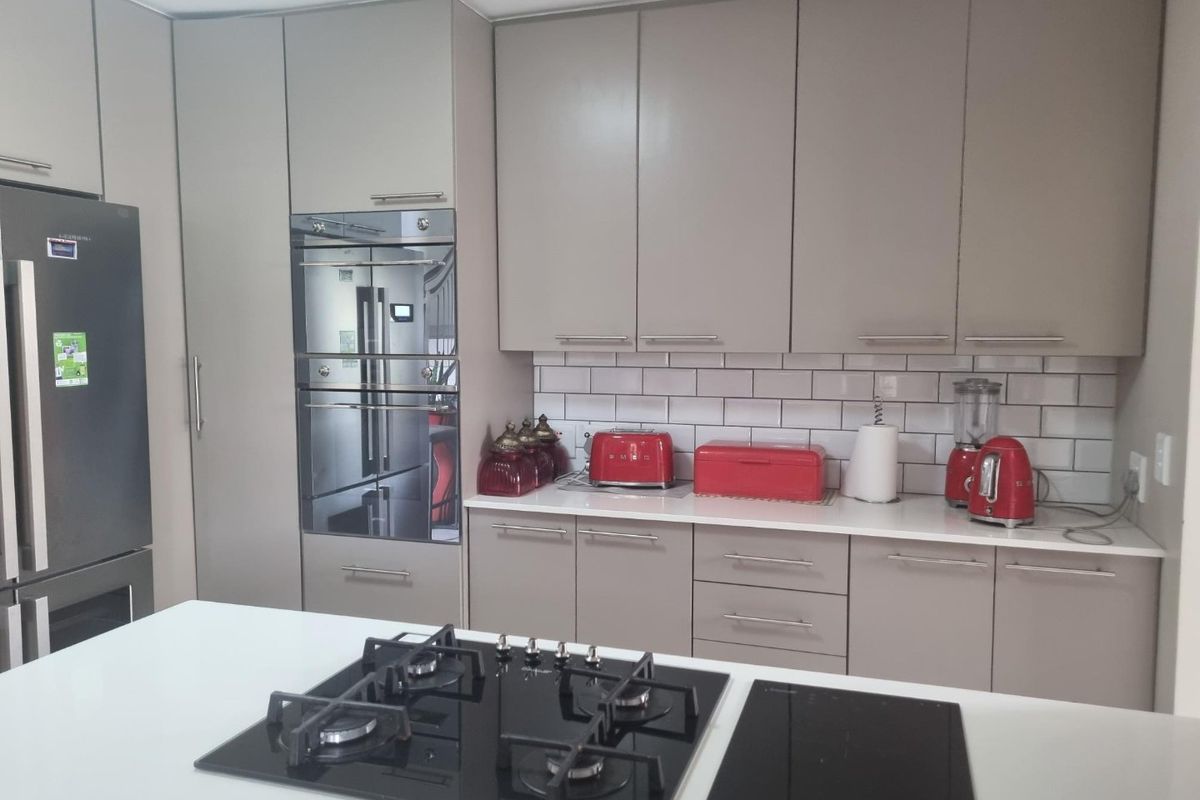Modern kitchen featuring sleek taupe cabinetry, stone countertops, subway tile backsplash, and a central island equipped with both gas and induction cooktops.