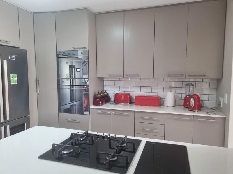 Modern kitchen featuring sleek taupe cabinetry, stone countertops, subway tile backsplash, and a central island equipped with both gas and induction cooktops.
