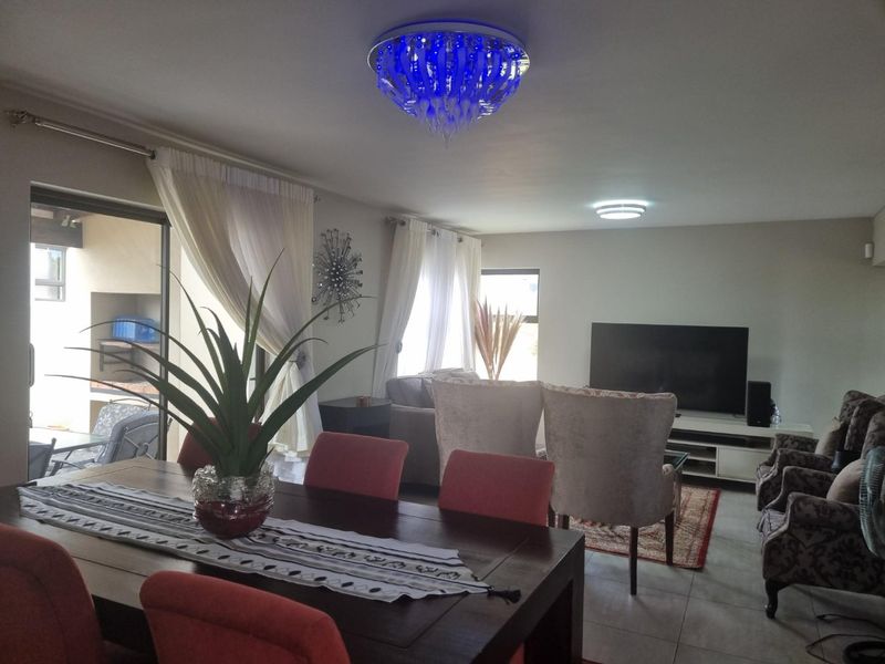 Spacious open-plan living and dining area featuring tiled flooring, large sliding doors leading to an outdoor patio, and modern lighting fixtures.