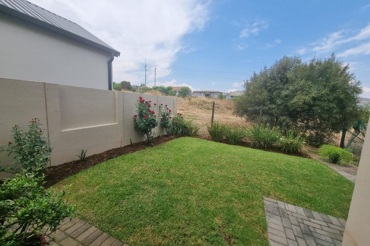 A well-maintained rear garden featuring a neat lawn, paved patio area, and a solid precast concrete boundary wall.