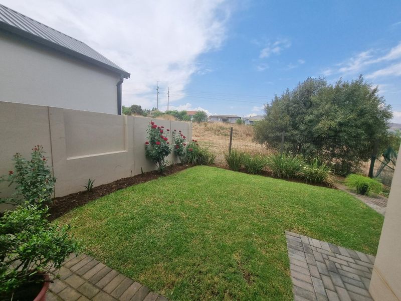 A well-maintained rear garden featuring a neat lawn, paved patio area, and a solid precast concrete boundary wall.