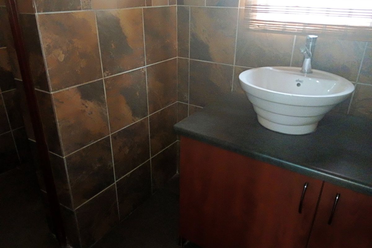 A bathroom vanity area featuring a vessel sink mounted on a dark countertop with decorative stone-look wall tiling.