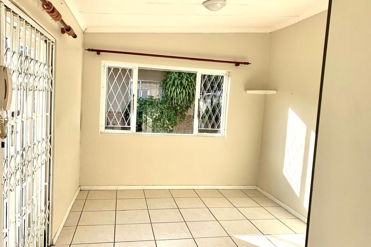 An empty living area featuring neutral tiled flooring, security gates, and window security bars, offering a clean, blank canvas for personalization.