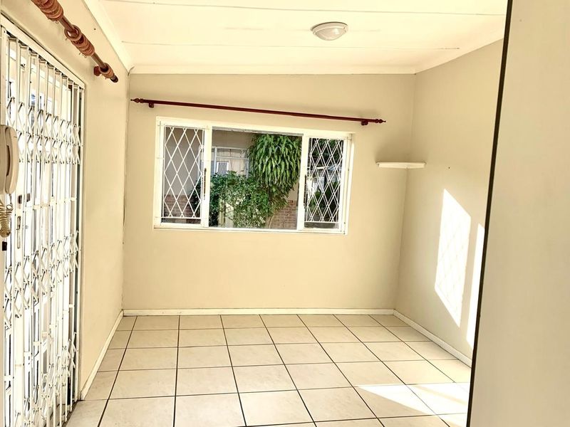 An empty living area featuring neutral tiled flooring, security gates, and window security bars, offering a clean, blank canvas for personalization.