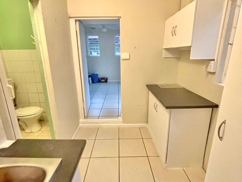 A compact kitchen area featuring built-in cabinetry, laminate countertops, and tiled flooring, with an adjacent bathroom and doorway leading to another room.