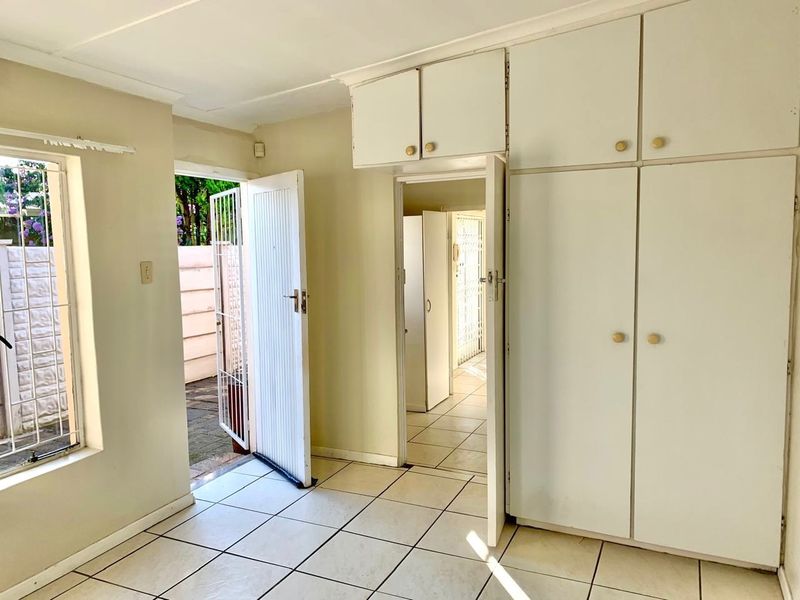 A vacant bedroom featuring built-in cupboards, tiled flooring, and direct access to an outdoor area through a security gate.