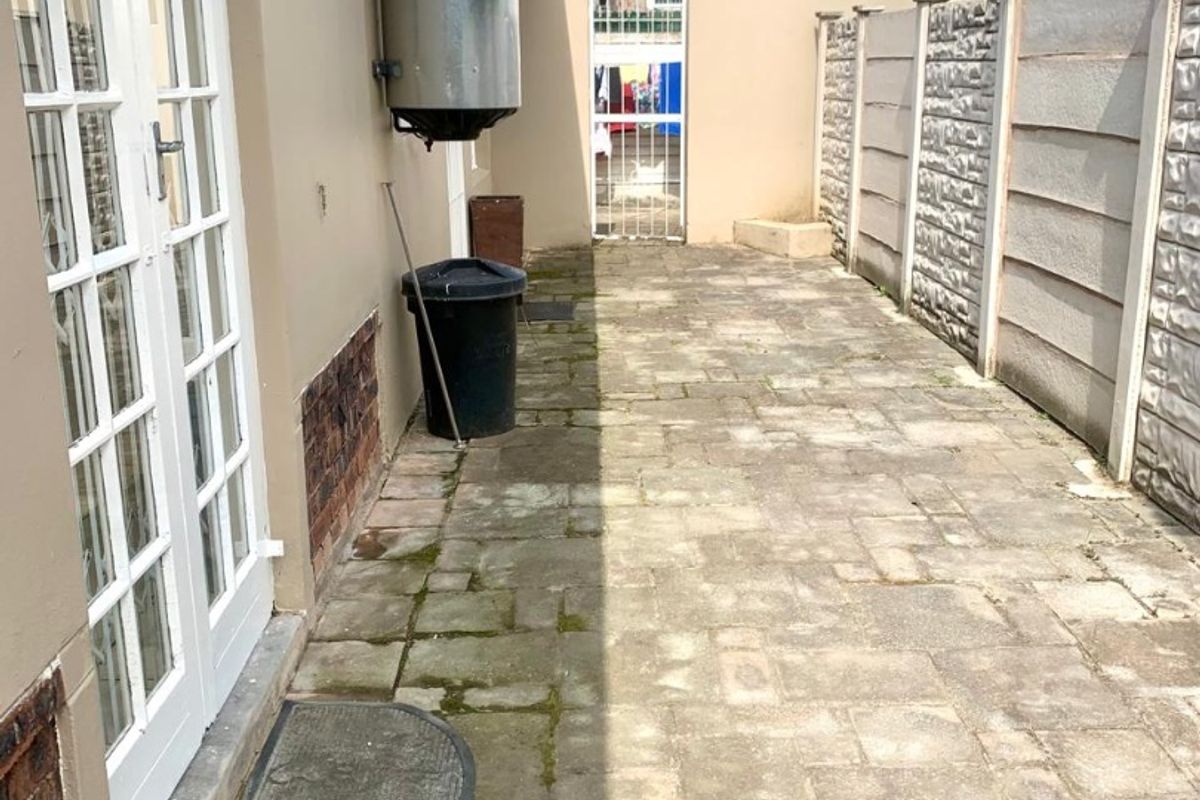 A paved rear courtyard area featuring a precast concrete boundary wall, external geyser unit, and access via white french doors.