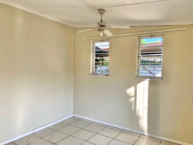 An empty bedroom featuring tiled flooring, a ceiling fan, and louver windows with security bars, offering a blank canvas for renovation.