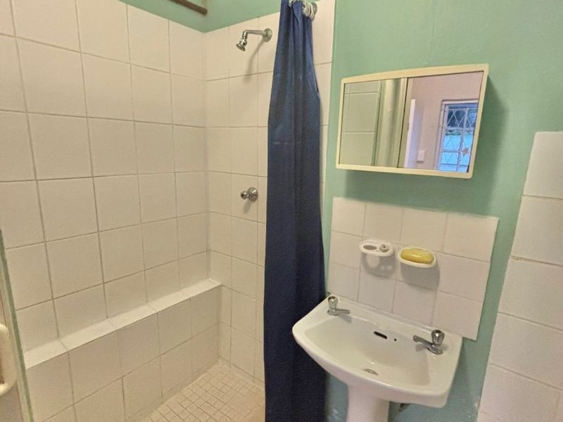 A functional bathroom featuring a pedestal washbasin, a tiled shower enclosure, and a wall-mounted medicine cabinet, requiring cosmetic updates to modernize the space.