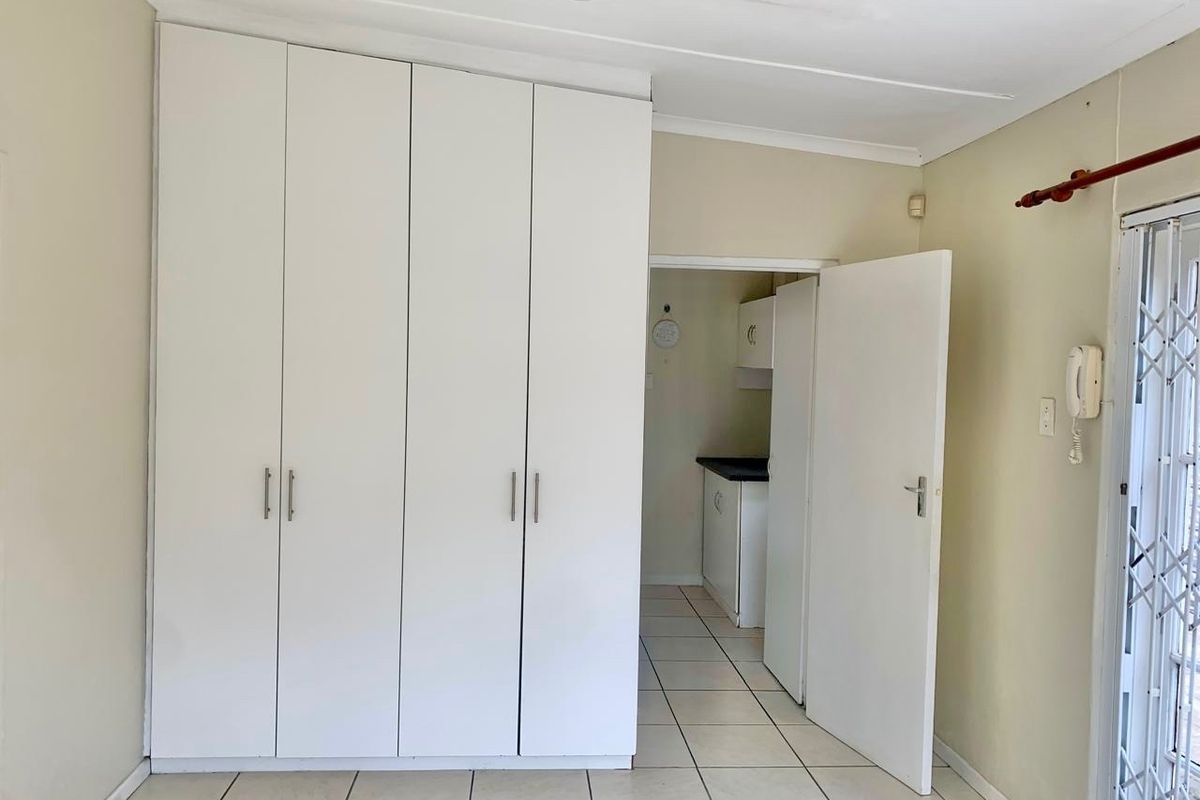 A clean, empty bedroom featuring white built-in cupboards, tiled flooring, and a security gate leading to an adjacent space.