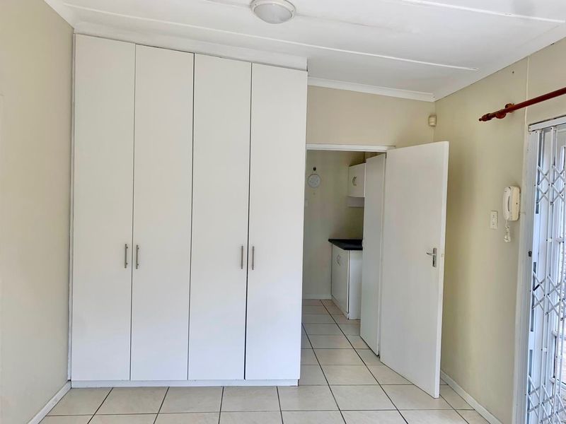A clean, empty bedroom featuring white built-in cupboards, tiled flooring, and a security gate leading to an adjacent space.