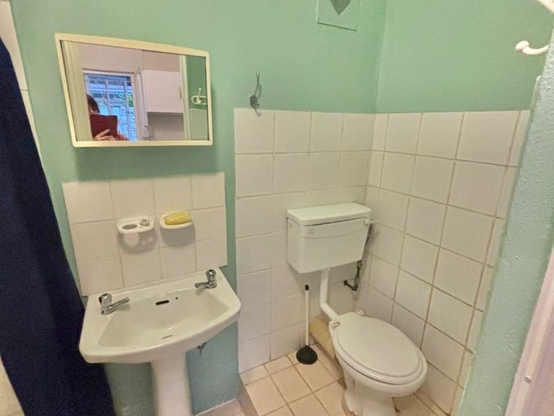 A compact bathroom featuring a pedestal washbasin and toilet with tiled flooring and splashbacks, requiring cosmetic updates to modernize the space.