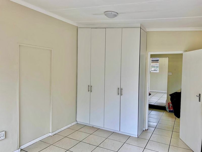 A bedroom featuring neutral walls, ceramic floor tiles, and a built-in white wardrobe, offering a clean and functional space ready for personalization.