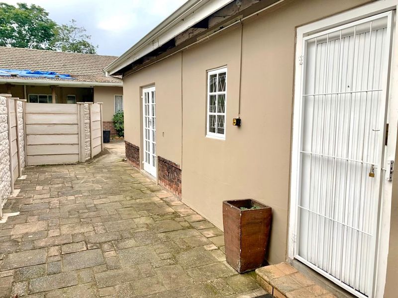 Rear exterior courtyard featuring paved flooring, security gates, and precast boundary walls, showing signs of weathering and maintenance requirements.
