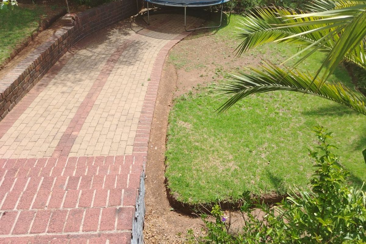 A rear garden featuring a paved walkway, brick retaining walls, and a lawn area, providing a functional outdoor space for the property.