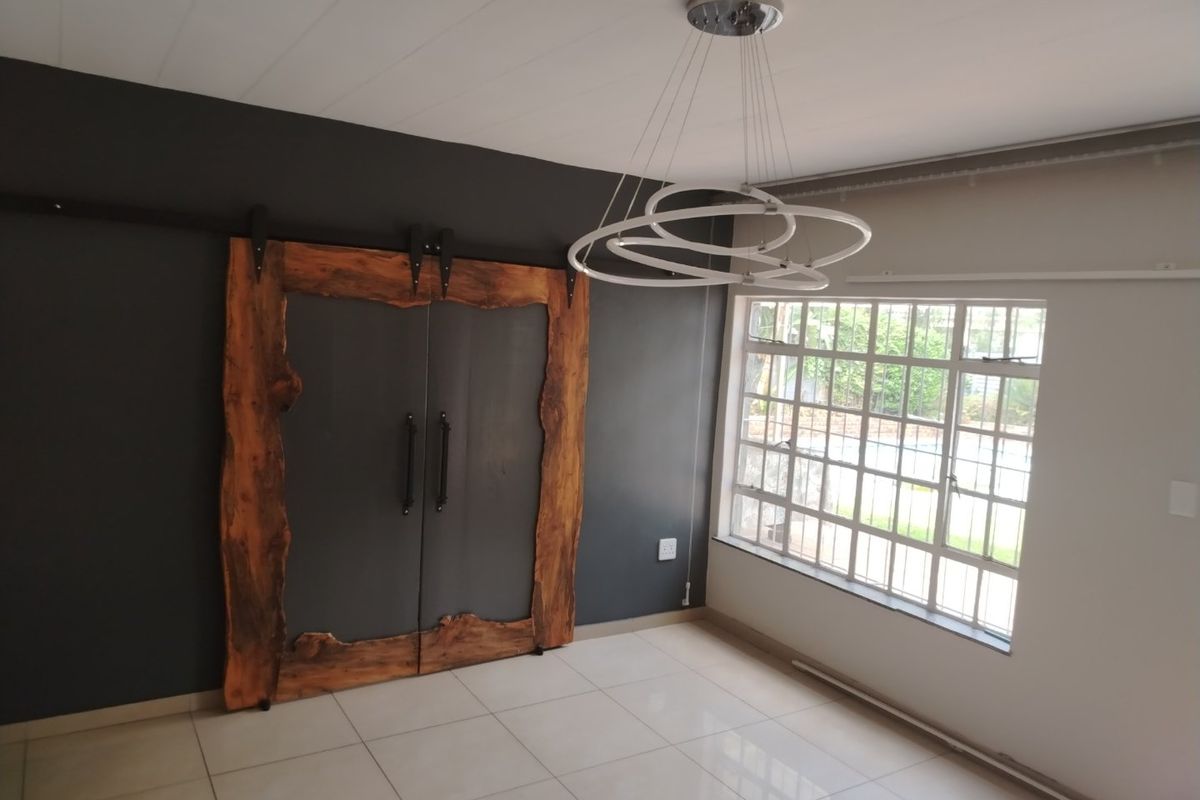 A bright, modern living space featuring large tiled flooring, a unique custom-framed sliding barn door, and a contemporary circular pendant light fixture.