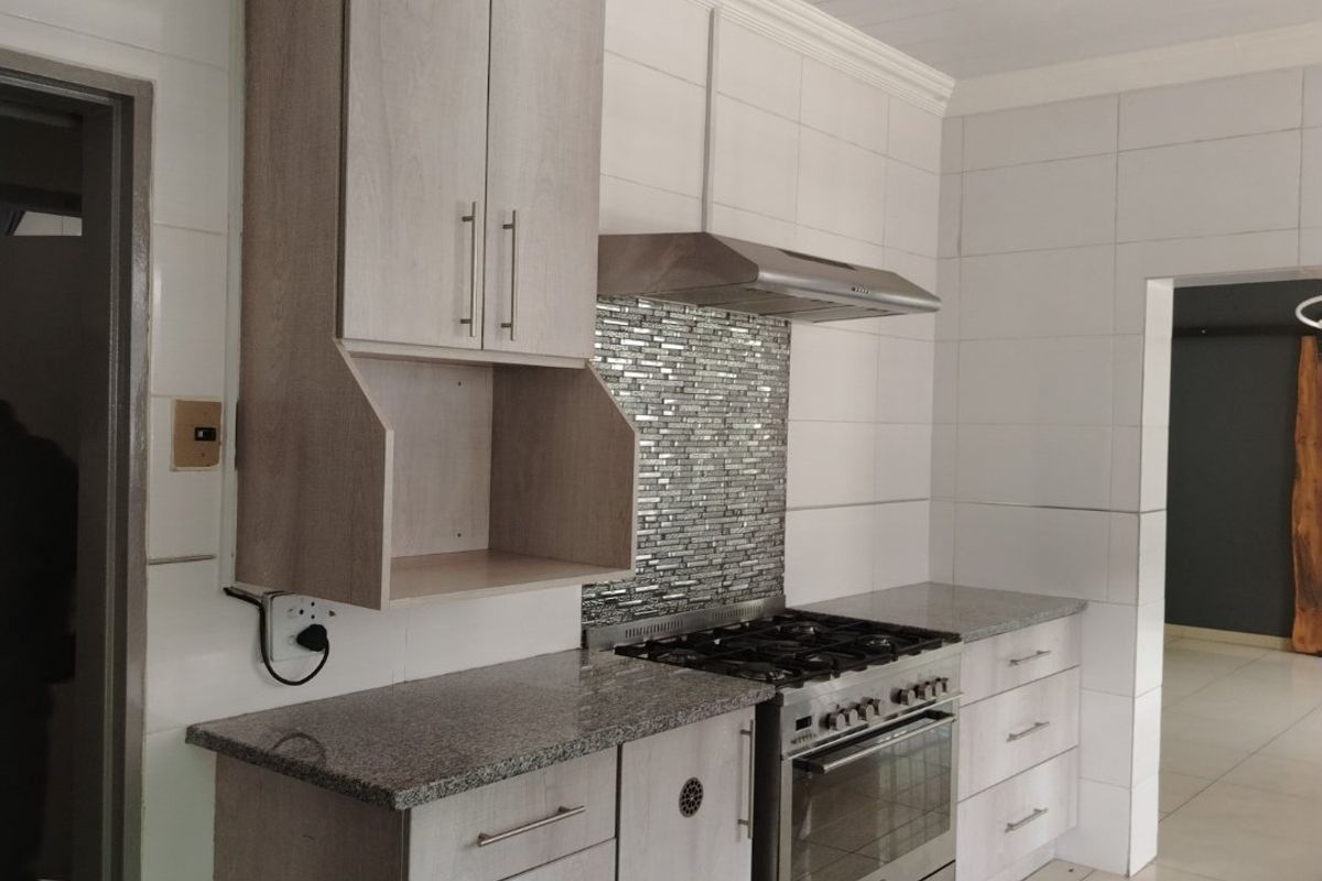 Modern kitchen featuring light wood cabinetry, granite countertops, a stainless steel gas stove with extractor fan, and a decorative mosaic tile backsplash.