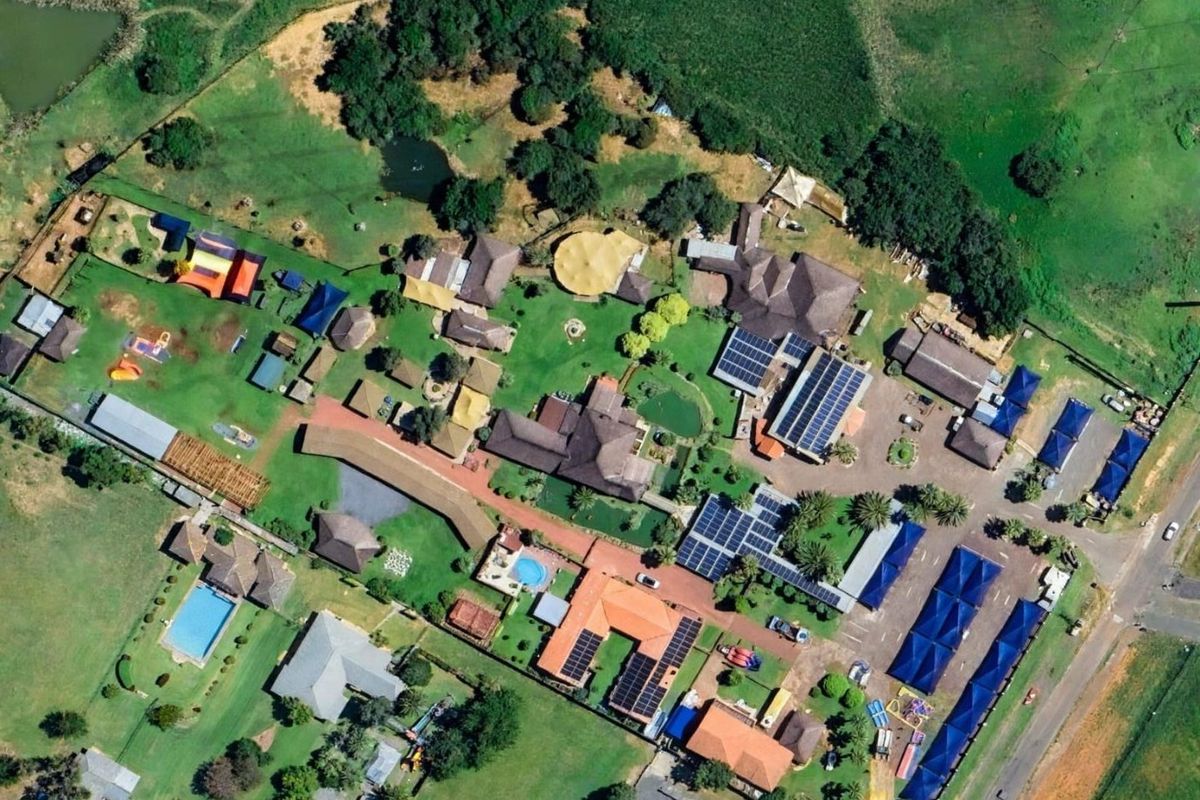 Aerial view of a commercial property complex featuring multiple buildings, solar panel installations, swimming pools, parking areas, and extensive landscaped grounds.