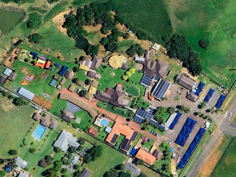 Aerial view of a commercial property complex featuring multiple buildings, solar panel installations, swimming pools, parking areas, and extensive landscaped grounds.