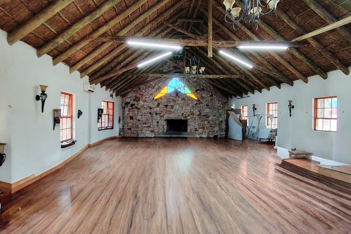 Spacious open-plan living area featuring a high vaulted thatched ceiling with exposed timber trusses, a prominent stone fireplace, and warm timber flooring.
